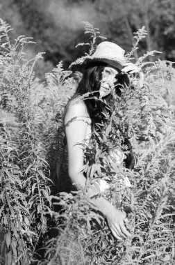 Yazlık giysiler içinde ve çayırda hasır şapkalı güzel bir kadının klasik fotoğrafı.