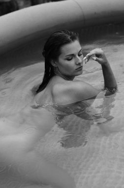 Yüzme havuzunda siyah beyaz pozlar veren mayolu, ıslak, güzel bir kadın. 