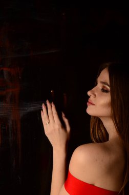 Stüdyoda kırmızı elbiseli güzel bir genç kız. Lüks mücevherler, kolyeler, yüzükler, parlak makyaj, kırmızı dudaklar, manikür. Büyüleyici lüks bayan..