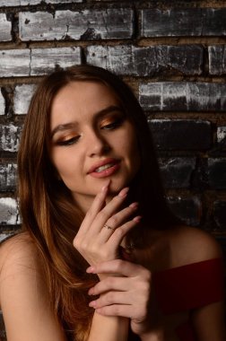 Stüdyoda kırmızı elbiseli güzel bir genç kız. Lüks mücevherler, kolyeler, yüzükler, parlak makyaj, kırmızı dudaklar, manikür. Büyüleyici lüks bayan..