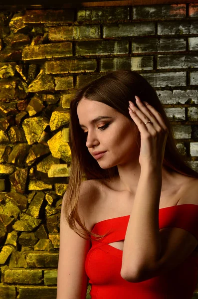 Stüdyoda kırmızı elbiseli güzel bir genç kız. Lüks mücevherler, kolyeler, yüzükler, parlak makyaj, kırmızı dudaklar, manikür. Büyüleyici lüks bayan..