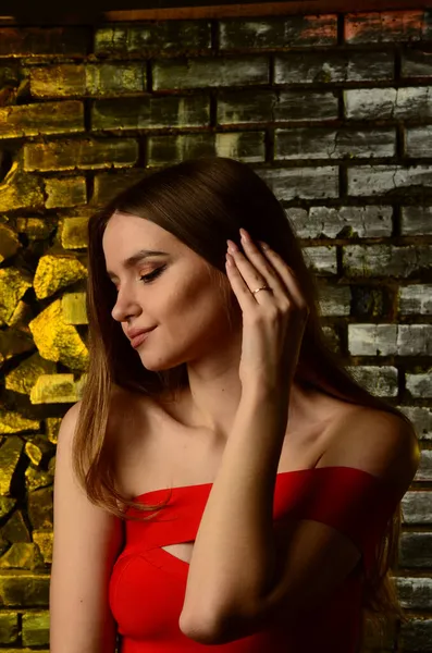 Stüdyoda kırmızı elbiseli güzel bir genç kız. Lüks mücevherler, kolyeler, yüzükler, parlak makyaj, kırmızı dudaklar, manikür. Büyüleyici lüks bayan..