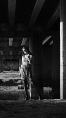 Bir sonbahar günü köprünün altında kameraya poz veren genç bir kadın. Siyah beyaz fotoğraf