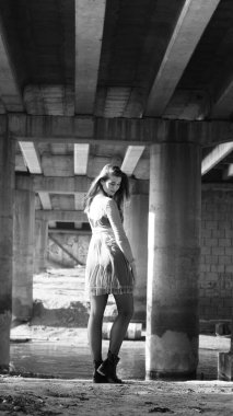 Bir sonbahar günü köprünün altında kameraya poz veren genç bir kadın. Siyah beyaz fotoğraf