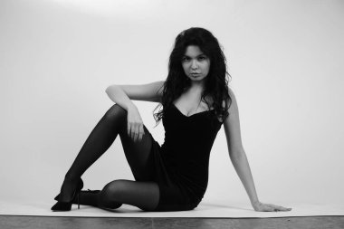 Siyah elbiseli güzel bir kadının siyah beyaz portresi stüdyoda poz veriyor.