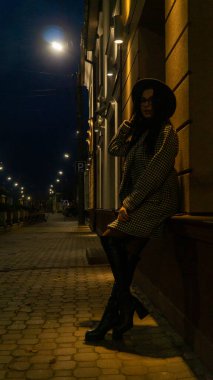 Siyah şapkalı genç ve güzel bir kız gece şehirde yürüyor ve kameraya poz veriyor.