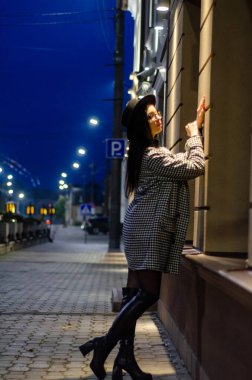 Siyah şapkalı genç ve güzel bir kız gece şehirde yürüyor ve kameraya poz veriyor.