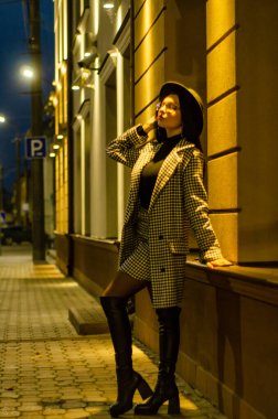 Siyah şapkalı genç ve güzel bir kız gece şehirde yürüyor ve kameraya poz veriyor.