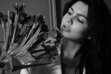 İç çamaşırlı ve ceketli güzel seksi bir kız elinde çiçeklerle stüdyoda kameraya poz veriyor, siyah beyaz bir fotoğraf.