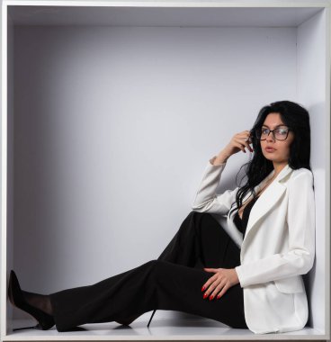 Beyaz odadaki kameraya poz veren siyah bluzlu ve beyaz ceketli çekici genç esmer manken.