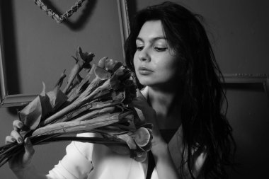 İç çamaşırlı ve ceketli güzel seksi bir kız elinde çiçeklerle stüdyoda kameraya poz veriyor, siyah beyaz bir fotoğraf.