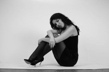 Siyah elbiseli güzel bir kadının siyah beyaz portresi stüdyoda poz veriyor.