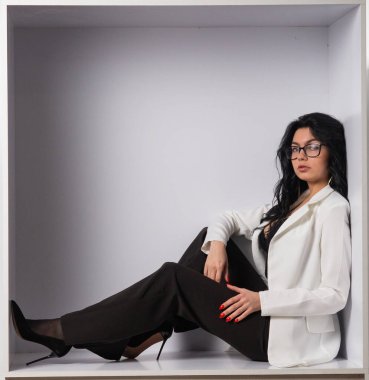 Beyaz odadaki kameraya poz veren siyah bluzlu ve beyaz ceketli çekici genç esmer manken.