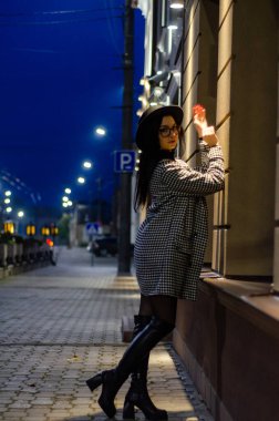 Siyah şapkalı genç ve güzel bir kız gece şehirde yürüyor ve kameraya poz veriyor.