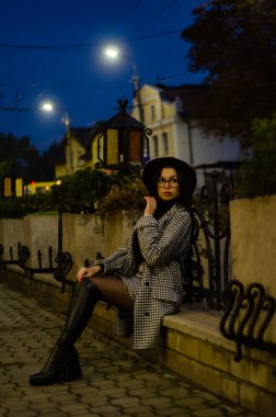 Siyah şapkalı genç ve güzel bir kız gece şehirde yürüyor ve kameraya poz veriyor.