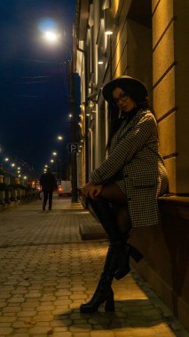 Siyah şapkalı genç ve güzel bir kız gece şehirde yürüyor ve kameraya poz veriyor.