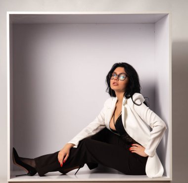 Beyaz odadaki kameraya poz veren siyah bluzlu ve beyaz ceketli çekici genç esmer manken.