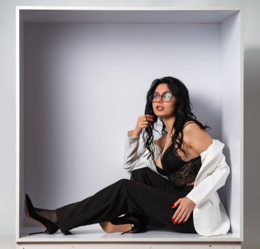 Beyaz odadaki kameraya poz veren siyah bluzlu ve beyaz ceketli çekici genç esmer manken.