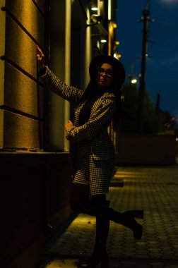 Siyah şapkalı genç ve güzel bir kız gece şehirde yürüyor ve kameraya poz veriyor.