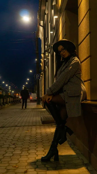 Siyah şapkalı genç ve güzel bir kız gece şehirde yürüyor ve kameraya poz veriyor.