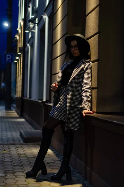 一个戴着黑色帽子的年轻漂亮的姑娘在夜城里散步 在镜头前摆姿势 — 图库照片