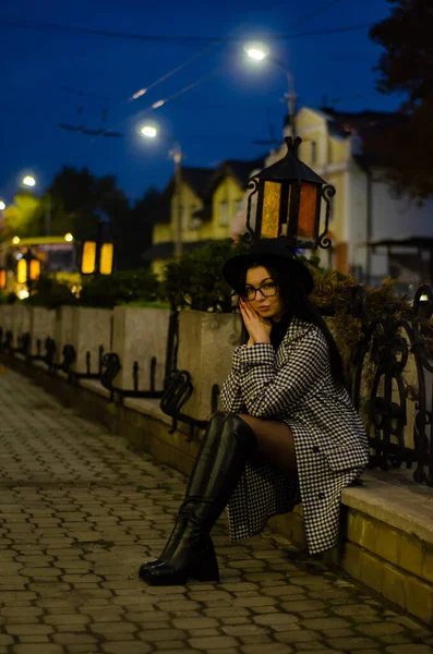 Siyah şapkalı genç ve güzel bir kız gece şehirde yürüyor ve kameraya poz veriyor.