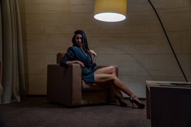 Siyah ceketli güzel bir kadın bir odada koltukta poz veriyor.