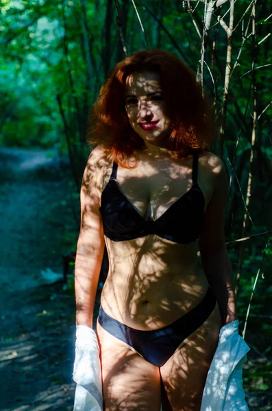 緑の夏の森に身を包んだ黒いランジェリー姿の美しい若い女性 — ストック写真