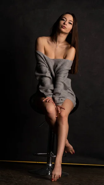 Hermosa chica sexy, con un vestido gris corto, silla de fondo negro. —  Fotos de Stock