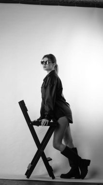 Siyah gömlekli ve güneş gözlüklü genç bir kadının stüdyoda poz verirken çekilmiş siyah beyaz bir fotoğrafı..  