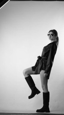 Siyah gömlekli ve güneş gözlüklü genç bir kadının stüdyoda poz verirken çekilmiş siyah beyaz bir fotoğrafı..  