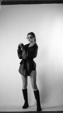 Siyah gömlekli ve güneş gözlüklü genç bir kadının stüdyoda poz verirken çekilmiş siyah beyaz bir fotoğrafı..  