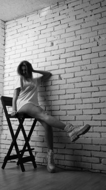 Stüdyoda sandalyenin yanında uzun saçlı, siyah beyaz bir kadın poz veriyor..  