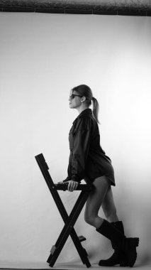 Siyah gömlekli ve güneş gözlüklü genç bir kadının stüdyoda poz verirken çekilmiş siyah beyaz bir fotoğrafı..  