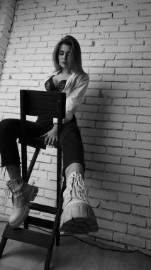 Beyaz tişörtlü, siyah beyaz saçlı, güzel ve seksi bir kadının stüdyoda beyaz bir duvara poz verdiği siyah beyaz bir fotoğraf..  