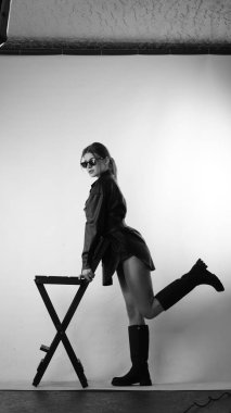 Siyah gömlekli ve güneş gözlüklü genç bir kadının stüdyoda poz verirken çekilmiş siyah beyaz bir fotoğrafı..  