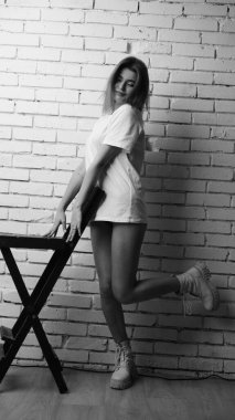 Stüdyoda sandalyenin yanında uzun saçlı, siyah beyaz bir kadın poz veriyor..  