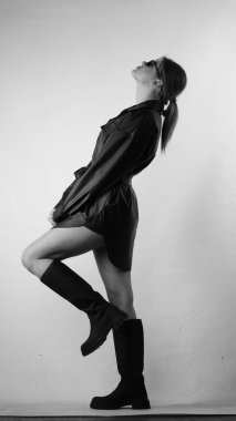 Siyah gömlekli ve güneş gözlüklü genç bir kadının stüdyoda poz verirken çekilmiş siyah beyaz bir fotoğrafı..  