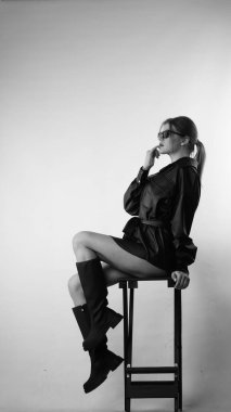 Siyah gömlekli ve güneş gözlüklü genç bir kadının stüdyoda poz verirken çekilmiş siyah beyaz bir fotoğrafı..  