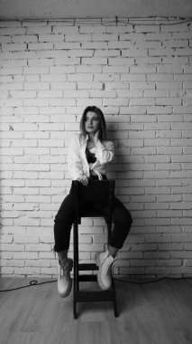 Beyaz tişörtlü, siyah beyaz saçlı, güzel ve seksi bir kadının stüdyoda beyaz bir duvara poz verdiği siyah beyaz bir fotoğraf..  