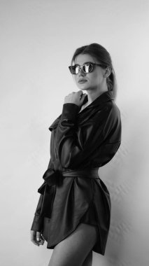 Siyah gömlekli ve güneş gözlüklü genç bir kadının stüdyoda poz verirken çekilmiş siyah beyaz bir fotoğrafı..  