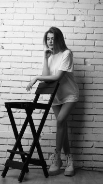Stüdyoda sandalyenin yanında uzun saçlı, siyah beyaz bir kadın poz veriyor..  