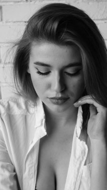 Beyaz tişörtlü, siyah beyaz saçlı, güzel ve seksi bir kadının stüdyoda beyaz bir duvara poz verdiği siyah beyaz bir fotoğraf..  