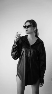 Siyah gömlekli ve güneş gözlüklü genç bir kadının stüdyoda poz verirken çekilmiş siyah beyaz bir fotoğrafı..  