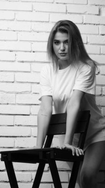 Stüdyoda sandalyenin yanında uzun saçlı, siyah beyaz bir kadın poz veriyor..  