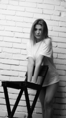 Stüdyoda sandalyenin yanında uzun saçlı, siyah beyaz bir kadın poz veriyor..  