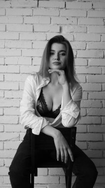 Beyaz tişörtlü, siyah beyaz saçlı, güzel ve seksi bir kadının stüdyoda beyaz bir duvara poz verdiği siyah beyaz bir fotoğraf..  