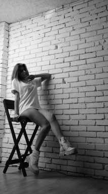 Stüdyoda sandalyenin yanında uzun saçlı, siyah beyaz bir kadın poz veriyor..  