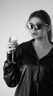 Siyah gömlekli ve güneş gözlüklü genç bir kadının stüdyoda poz verirken çekilmiş siyah beyaz bir fotoğrafı..  