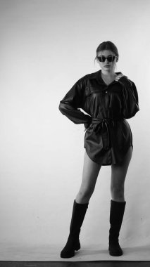 Siyah gömlekli ve güneş gözlüklü genç bir kadının stüdyoda poz verirken çekilmiş siyah beyaz bir fotoğrafı..  